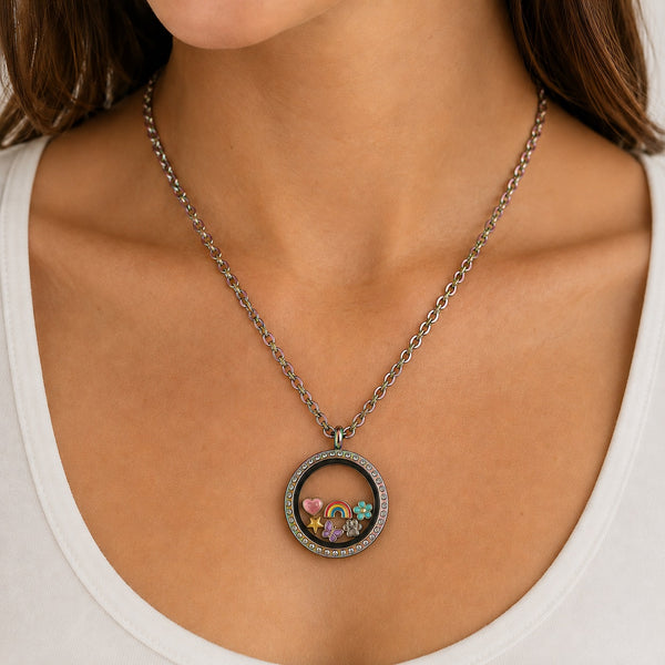 A close-up of a woman wearing a round floating charm locket necklace. The locket features a rainbow finish with clear crystals around the locket and small colorful charms sinside, including a rainbow, heart, star, flower and paw print.