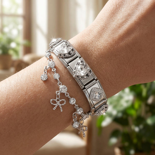 Silver 9mm Italian charm bracelet with heart and bow charms on a wrist, blurred indoor background