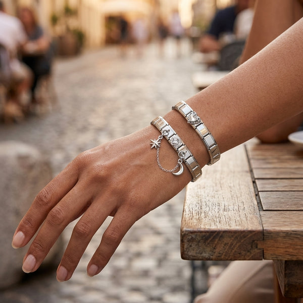 Hand wearing multiple 9mm Italian charm bracelets with accent chain in silver with star and moon charms on a blurred outdoor background