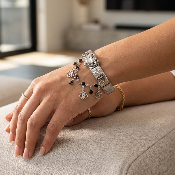 Person wearing silver 9mm Italian charm bracelet connector with black bead and floral drop charms on a blurred indoor background