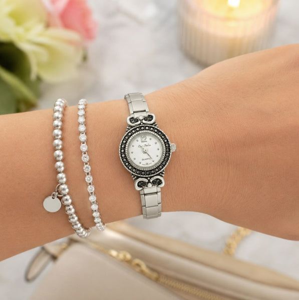 A 9mm Italian charm antiqued women's watch with a black crystal-accented bezel, shown worn on a wrist alongside two pearl beaded bracelets.