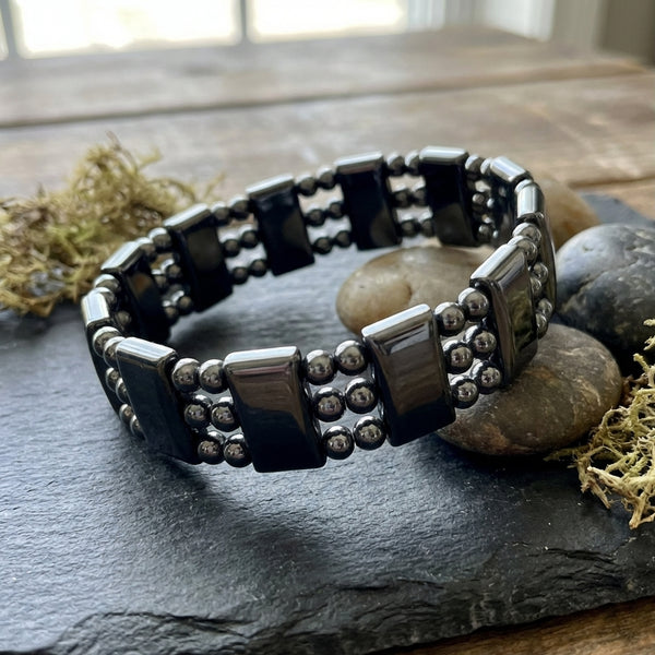 Black beaded magnetic hematite bracelet on a dark surface with stones and moss