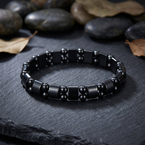 Black magnetic hematite beaded bracelet on a dark surface with rocks and leaves in the background