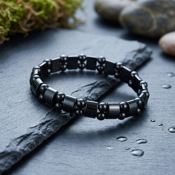 Black beaded hematite bracelet on a dark stone surface with water droplets