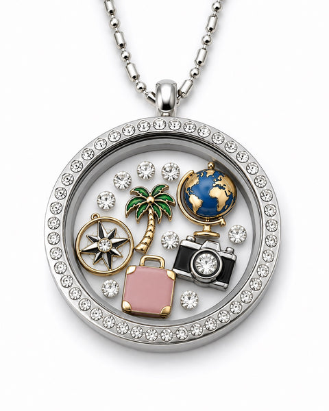 A silver round floating charm locket necklace with a bezel-set crystal border, featuring charms of a pink suitcase, camera, globe, palm tree, compass, and rhinestones on a white background.