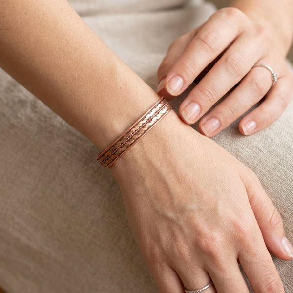 Close-up of a hand wearing a copper cuff bracelet on a neutral background