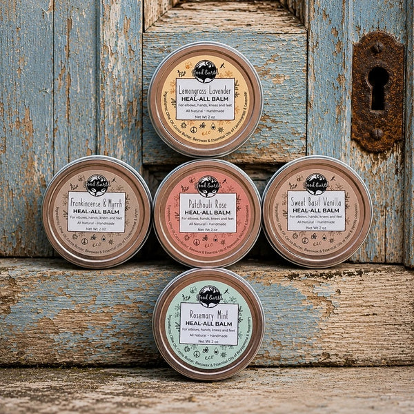 Five Good Earth Soap Co. Heal All Balm 2 oz tins in Lemongrass Lavender, Frankincense & Myrrh, Patchouli Rose, Sweet Basil Vanilla, and Rosemary Mint displayed on a rustic wooden background.