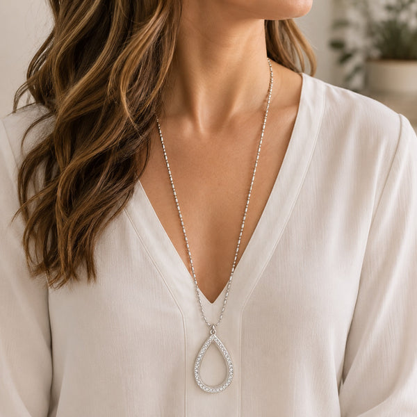 A close-up of a woman wearing a teardrop-shaped floating charm locket necklace encrusted with small clear stones.