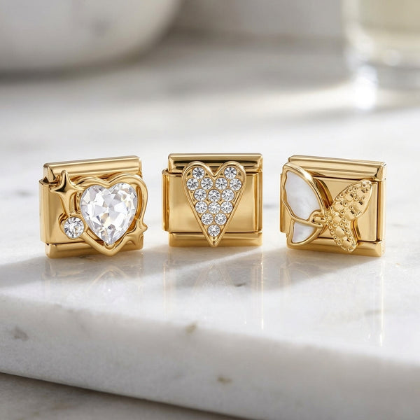 Three gold 9mm Italian charms with heart and butterfly designs on a marble surface
