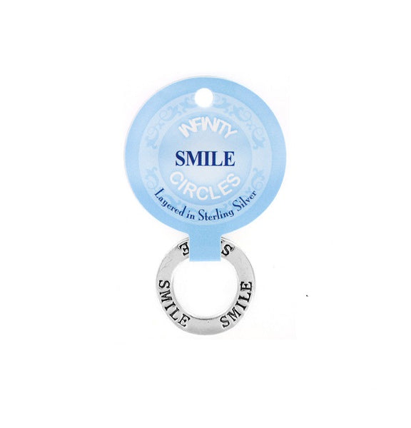 A silver plated infinity circle token chip engraved with the word 'SMILE' on both sides, attached to a light blue circular paper tag that reads 'INFINTY CIRCLES' and 'Layered in Sterling Silver'.